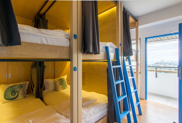 Een slaapkamer met stapelbedden, een houten inrichting, een blauwe ladder en uitzicht op de stad door een groot raam.