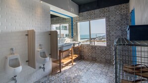 A modern bathroom with white urinals, a sink, and a mirror. There is a window with a view of the sea.