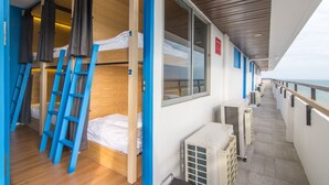 A corridor with bunk beds, a blue ladder, and a window with a view of the sea.