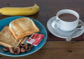 Een bord met toast en chocolade chips, een banaan en een kop koffie op een houten tafel.