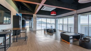 An open-plan office with wooden flooring, black and grey furniture, and large windows offering a view of a bridge and water.