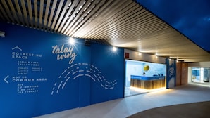 A modern hotel interior with a reception desk, a blue wall with directional signs, and a wooden ceiling.