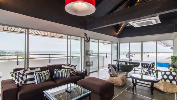Uma sala de estar moderna com um sofá, uma mesa de centro de vidro e uma luminária pendente vermelha.
