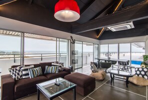 Uma sala de estar moderna com um sofá, uma mesa de centro de vidro e uma luminária pendente vermelha.