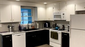 Une cuisine avec des meubles blancs, un plan de travail noir, un four à micro-ondes, une cuisinière et un lave-vaisselle.