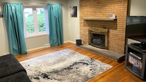 Un salon avec une cheminée, un plancher en bois, un canapé noir et des rideaux turquoise.