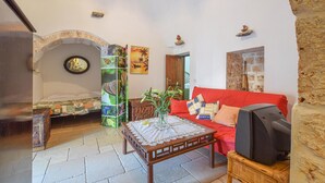 Ein gemütliches Wohnzimmer mit einem roten Sofa, einem Fernseher, einem dekorativen Tisch und einem markanten Steingewölbe.