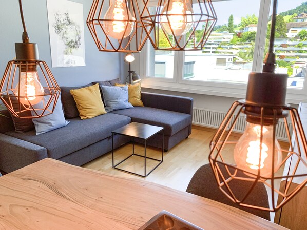 Ein modernes Wohnzimmer mit Ecksofa, Couchtisch und Pendelleuchten.