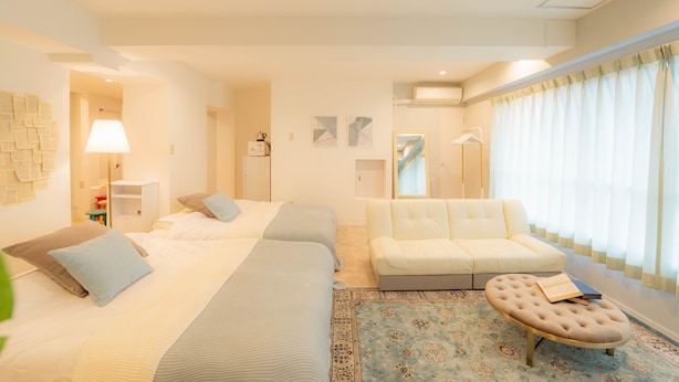 A hotel room with two beds, a sofa, a small table, and a window with curtains. - Swwitch House Central Tokyo 7 (Tokyo)