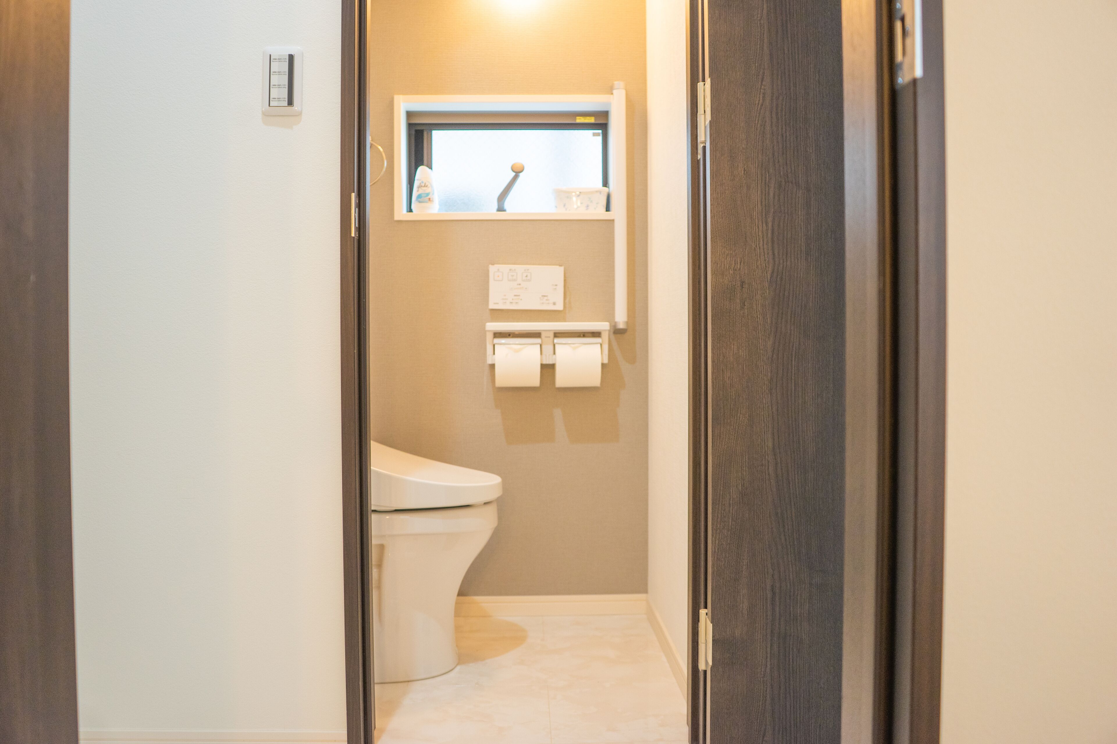 A narrow bathroom with a toilet, a small window, and a towel dispenser.