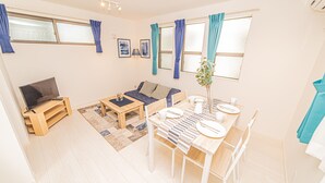 A modern living room with a flat-screen TV, sofa, coffee table, dining table with chairs, and a potted plant. - Sumida family hotel in Tokyo (Tokyo)