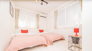 A room with two beds, a small table with a lamp, and an air conditioning unit. - Sumida family hotel in Tokyo (Tokyo)