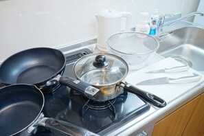 Une cuisine équipée d’une cuisinière, de casseroles, de poêles, d’une passoire, d’une bouilloire et de produits de nettoyage.