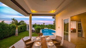 Zona pranzo all'aperto con vista su una piscina, immersa nel verde e circondata da un prato curato.