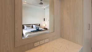 Una moderna camera d'hotel con un grande specchio, rivestimenti in legno, un piano di lavoro in marmo e un letto rifatto con un asciugamano blu.