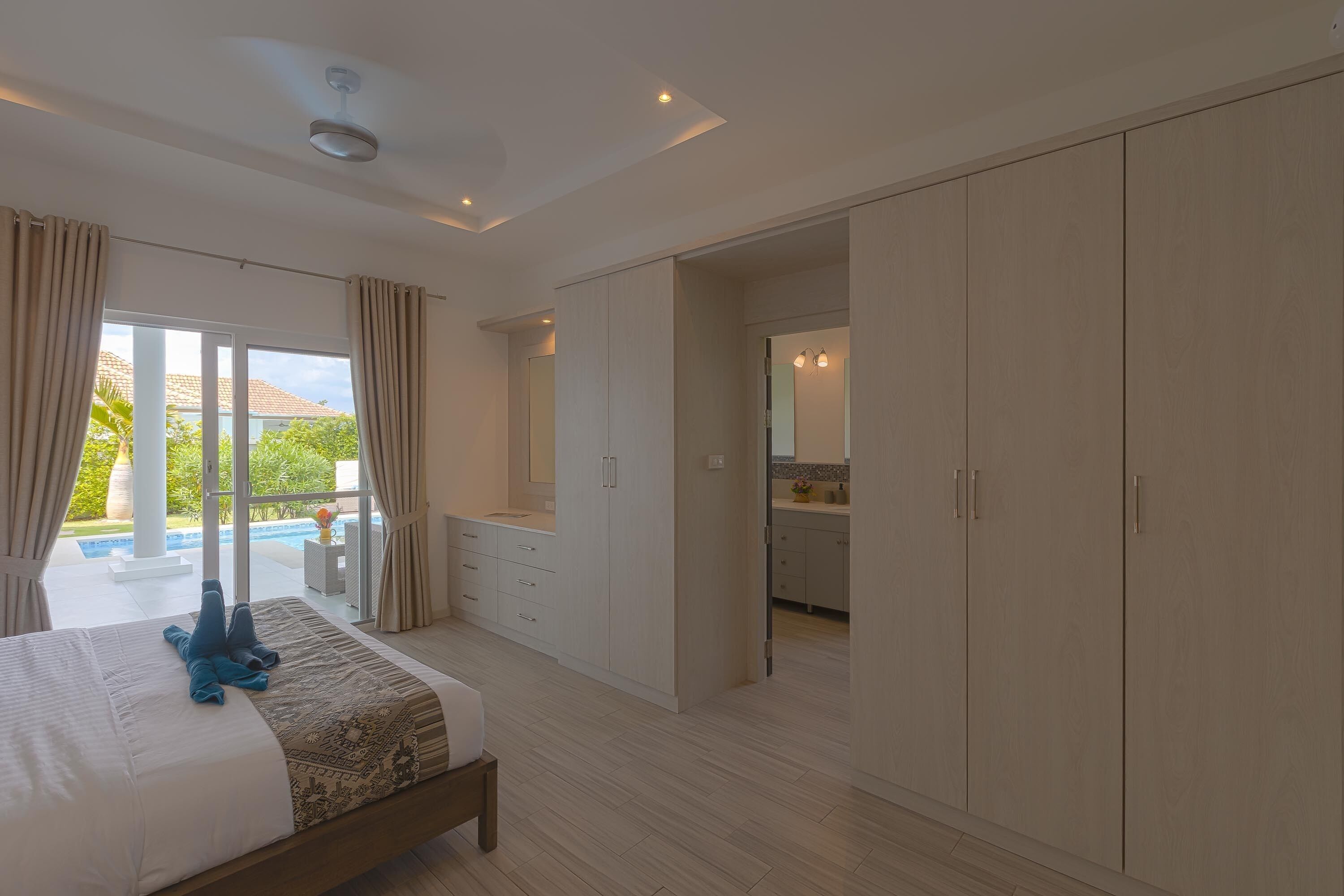 A bedroom with a large bed, a wardrobe, and a view of a pool and garden.