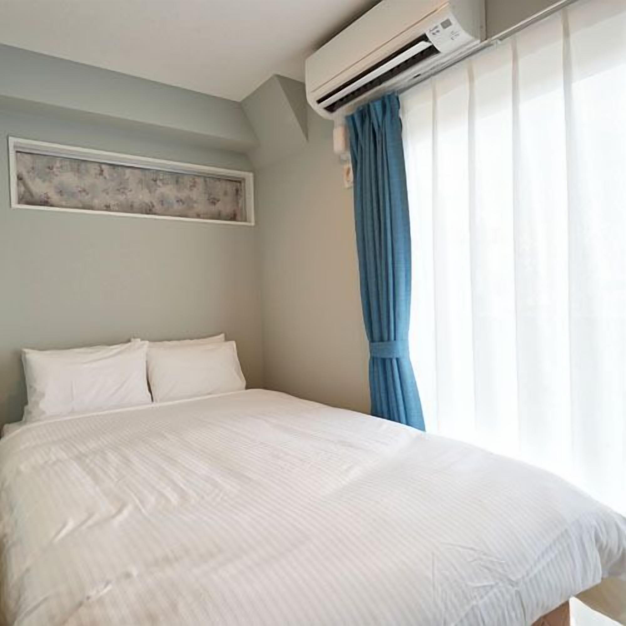 A bedroom with a bed, an air conditioning unit, a window with curtains, and a painting on the wall.
