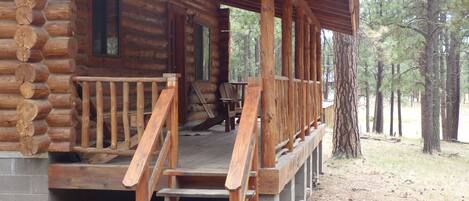 A log cabin with a wooden porch and steps leading to a deck.