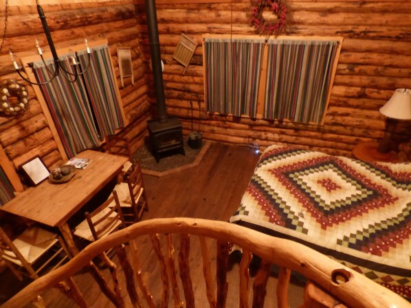 Interior acogedor de una cabaña de madera con una mesa, sillas, una cama acolchada, una chimenea y una ventana con cortina a rayas.