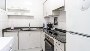 Une cuisine moderne avec des armoires blanches, un comptoir en granit, un four encastré, un four à micro-ondes et un lave-linge.
