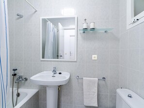 A bathroom with a white sink, a mirror, a towel rack, a glass shelf with toiletries, and a shower.
