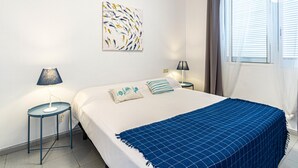 Une chambre à coucher comprenant un lit, deux tables de chevet, une lampe, une fenêtre avec des rideaux et une œuvre d’art murale.