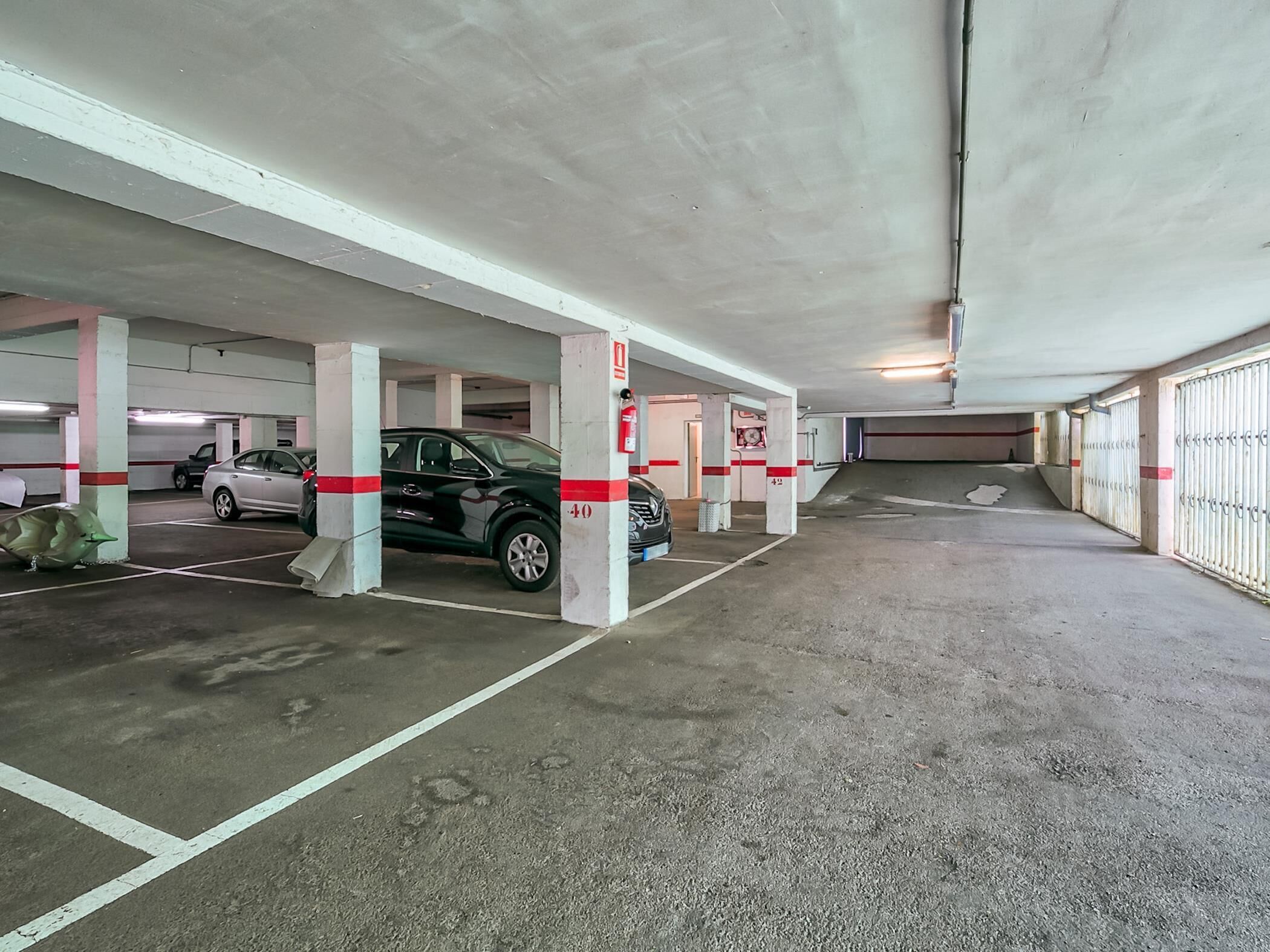 En underjordisk parkeringsgarage med flere niveauer, betondækstolper, markerede parkeringspladser og en brandslukker på en af stolperne.