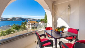 Un balcone con tavolo e sedie, vista sul mare e un edificio sullo sfondo.