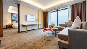 A modern hotel room with a sofa, a dining table, and a TV mounted on the wall.
