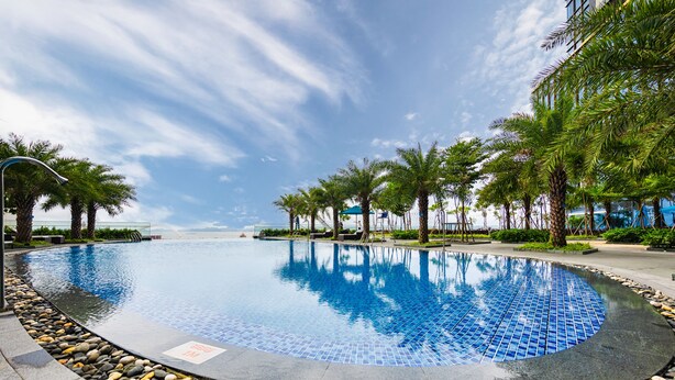 A circular infinity pool with a tiled edge, surrounded by palm trees and a pebble border.