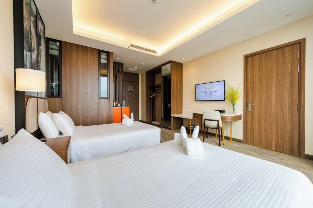 A hotel room with two beds, a desk, a chair, a TV, and a wardrobe.