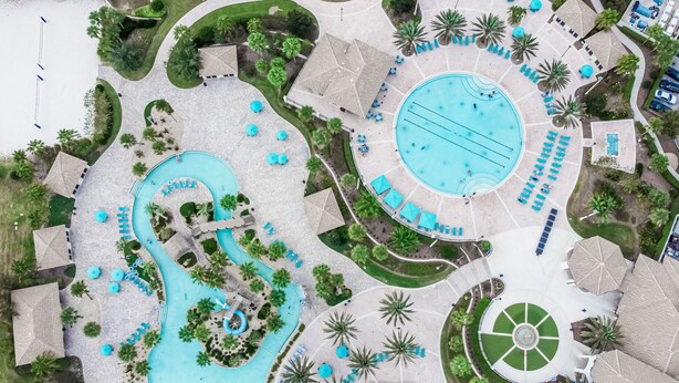 Eine Luftaufnahme eines Resorts mit mehreren Swimmingpools, Liegestühlen und Palmen.