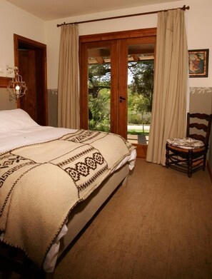 Une chambre à coucher avec un lit, une chaise, une porte, une fenêtre avec des rideaux et un tableau accroché au mur.