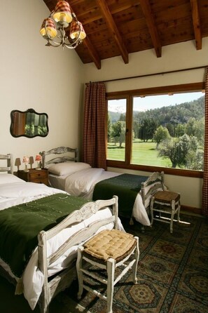 Une chambre avec deux lits, un plafond en bois, une grande fenêtre donnant sur les arbres et un tapis à motifs.