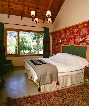 A bedroom with a large bed, a wooden ceiling, a window with curtains, and a patterned wall.