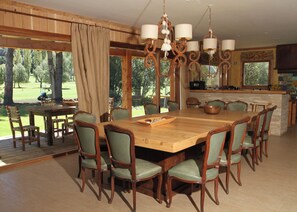 Un espace repas avec une grande table en bois, des chaises à revêtement vert et un lustre.