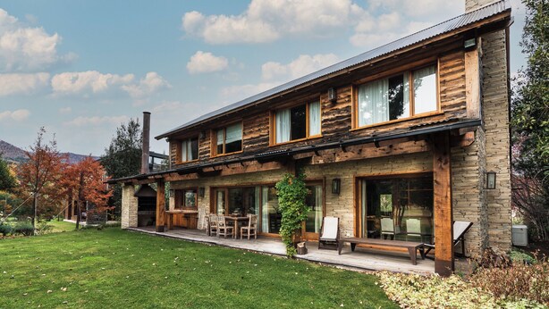 A two-story log cabin with a stone facade, large windows, and a covered patio area. - Alhue - Casa en el Golf (San Carlos de Bariloche)
