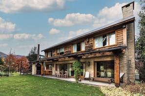 A two-story log cabin with a stone facade, large windows, and a covered patio area. - Alhue - Casa en el Golf (San Carlos de Bariloche)