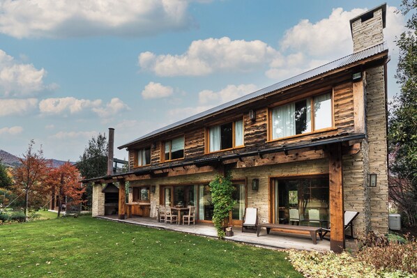 Une cabane en rondins à deux étages, dotée d’une façade en pierre, de grandes fenêtres et d’un patio couvert.