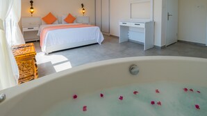 Une chambre à coucher avec une grande baignoire remplie de pétales de roses, un lit avec des oreillers orange, un bureau et une armoire.
