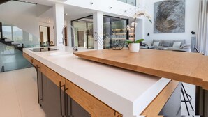 A modern kitchen with a central island, a dining area with a sofa, and a large window offering a view of the outdoors. - Montblau, luxury holiday villa (Buger)