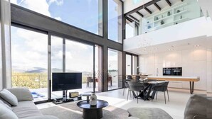 A modern living room with a large TV, comfortable seating, and a dining area with a kitchen in the background. - Montblau, luxury holiday villa (Buger)