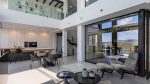 A modern, open-plan living area with a kitchen, dining space, and a seating area with a view. - Montblau, luxury holiday villa (Buger)