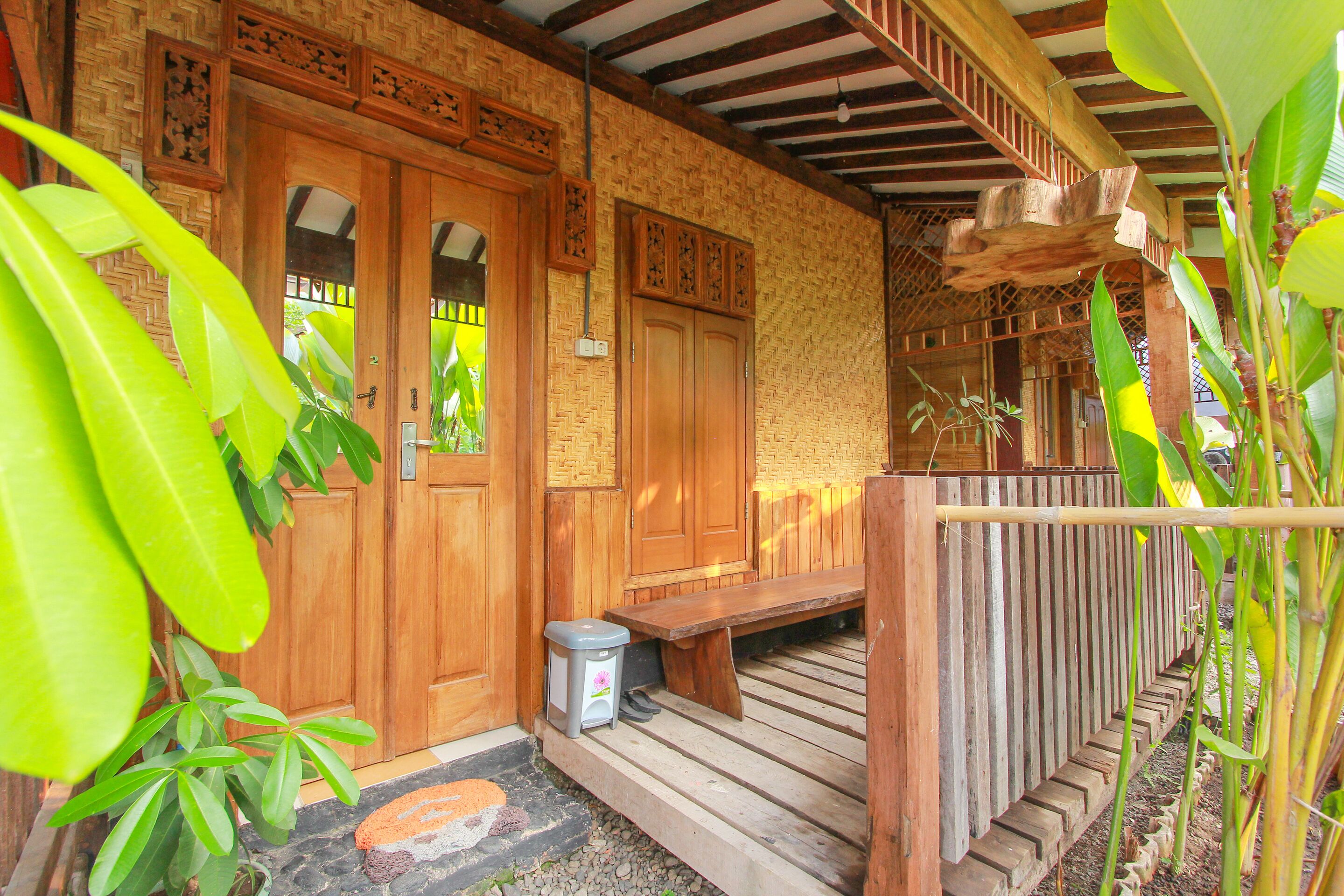 Une véranda en bois avec un banc, une poubelle et une porte ornée de panneaux décoratifs.