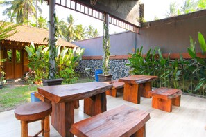 An outdoor patio with wooden tables and benches, surrounded by potted plants and a stone wall.