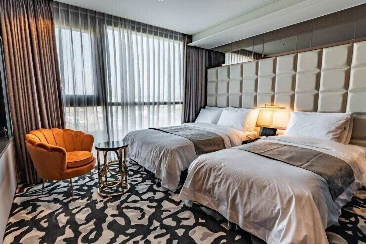 A hotel room with two beds, a small round table, a chair, and a patterned carpet.