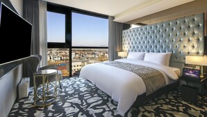 A hotel room with a large bed, a TV, a desk, and a view of a cityscape. - Best Louis Hamilton Hotel West Busan (Busan)