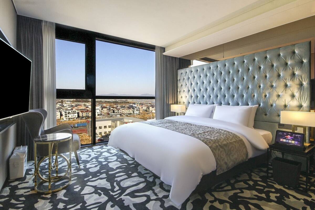 A hotel room with a large bed, a TV, a desk, and a view of a cityscape.