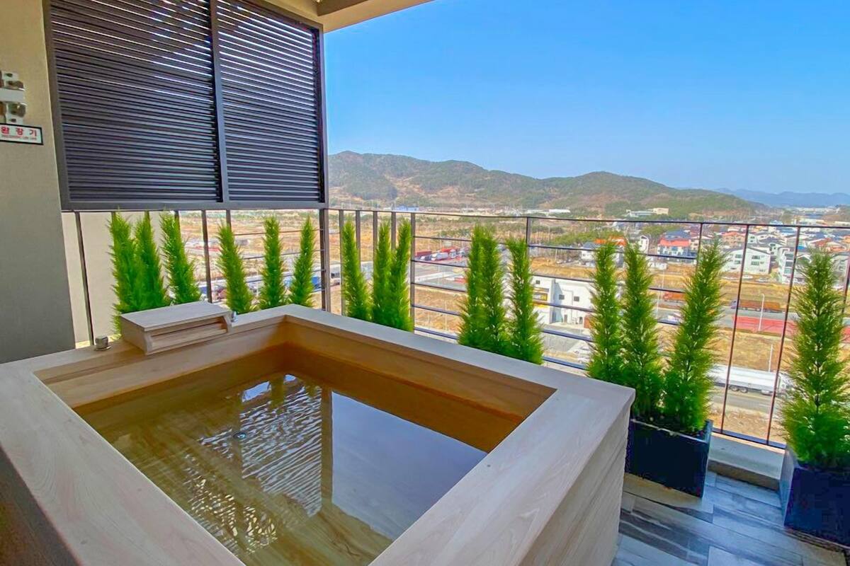 A balcony with a hot tub, potted plants, and a view of a cityscape and mountains.
