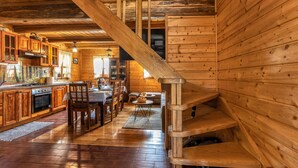 Interior de una cabaña de madera con cocina, comedor y una escalera de madera.